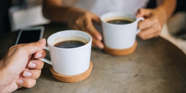 Close up woman and man holding cups of coffee on table